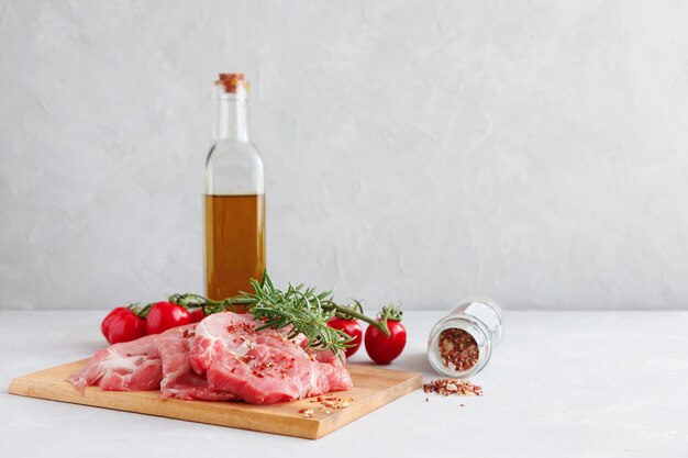 Foto bistecche di maiale su una tavola di legno, sullo sfondo una bottiglia con olio d'oliva, pomodorini e spezie