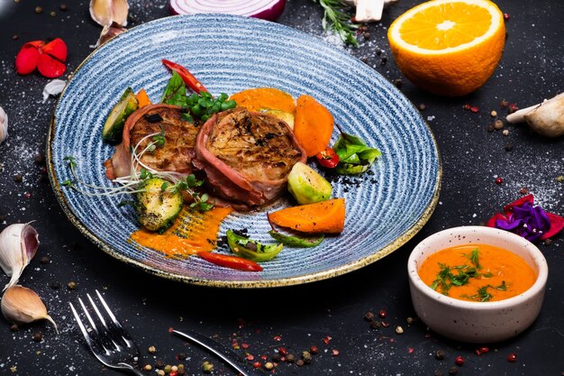 Pork tenderloin medallions in bacon with spicy sauce and brussels sprouts, on dark surface