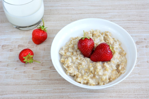 porridge in white bowl with strawberry isolated with glass of milk, close-up