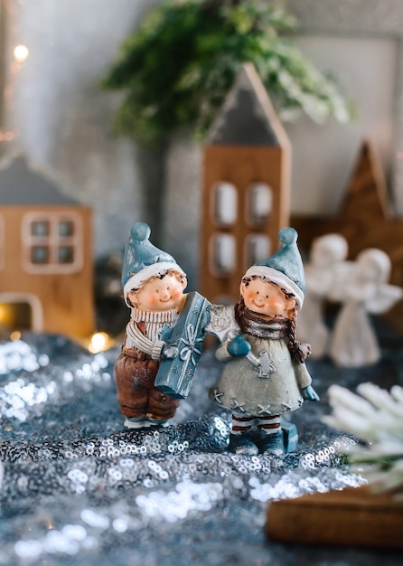 Porseleinen beeldjes van kinderen in een kerstdecor. Winterbeeldjes van een jongen en een meisje met geschenken op de achtergrond van huizen en kegels. Kerst wenskaart. Ruimte kopiëren.