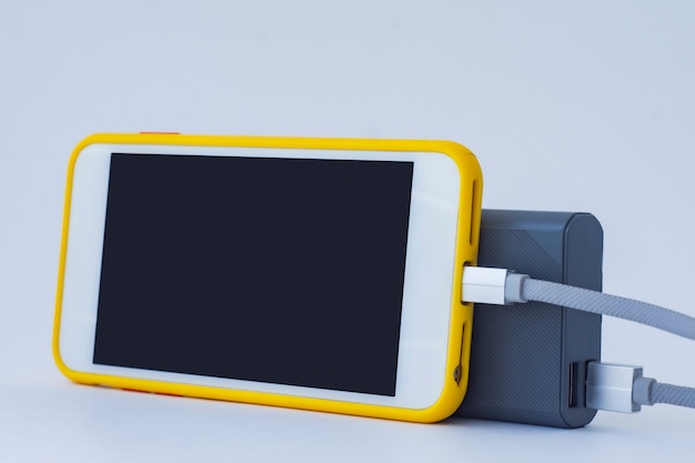 Foto il caricabatterie portatile carica uno smartphone isolato su uno sfondo bianco. mockup di telefono cellulare con schermo bianco e power bank.