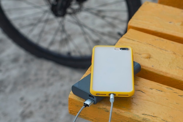 ポータブル充電器は、木製のベンチと自転車を背景にケーブルでスマートフォンのパワーバンクを充電します