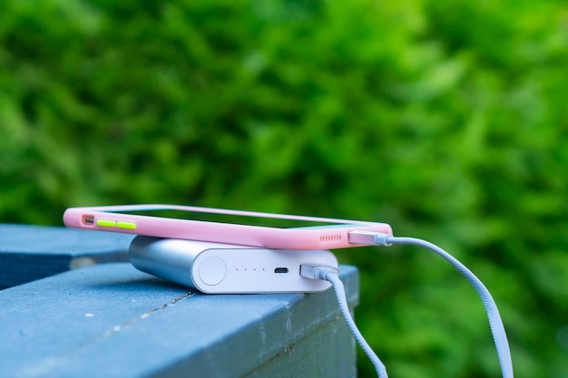 Portable charger charges a smartphone on a wooden railing. Mobile phone mockup with dark screen and power bank.