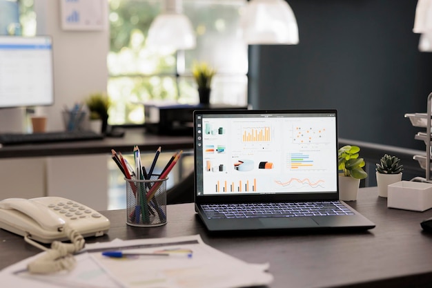 Portable computer with main management program on screen on\
modern office desk. laptop display statistics and financial results\
with profit and investment reports, inside workplace.