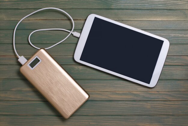 Portable power bank and tablet PC on wooden background