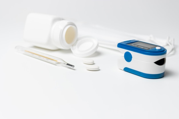 Portable pulse oximeter, thermometer and pills on white background