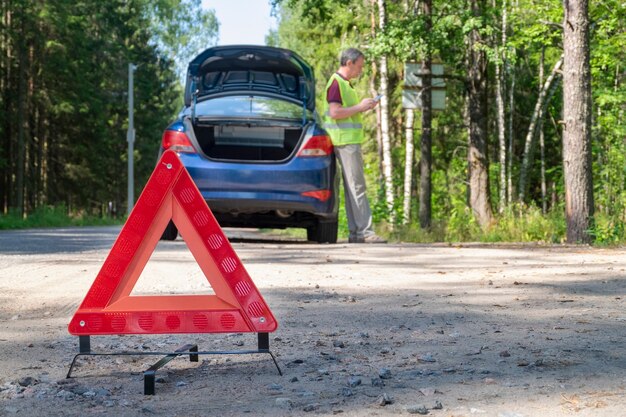 Portable warning triangular sign on the side of rural road near a car