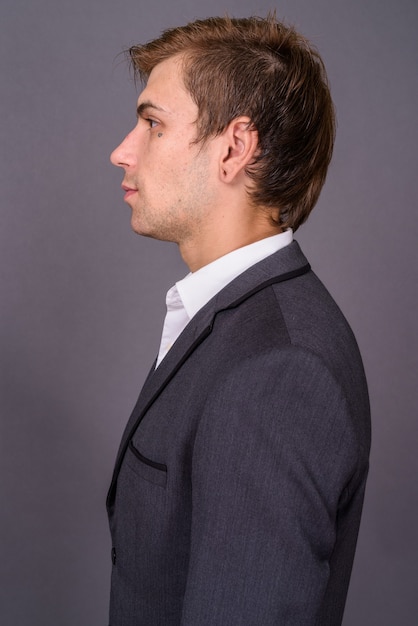 Portait of young handsome businessman against gray wall