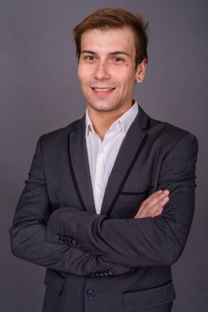 Portait of young handsome businessman against gray wall