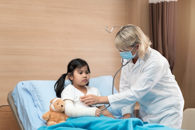 Portarit of smaile doctor pediatrician and little girl patient on bed with teddy bear