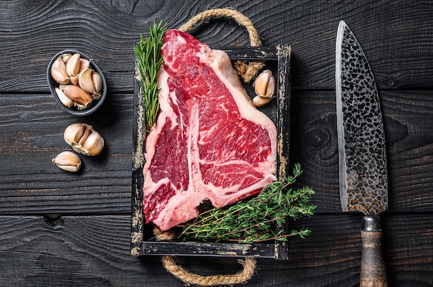 Porterhouse or T bone raw beef meat Steak with herbs and salt in wooden tray.