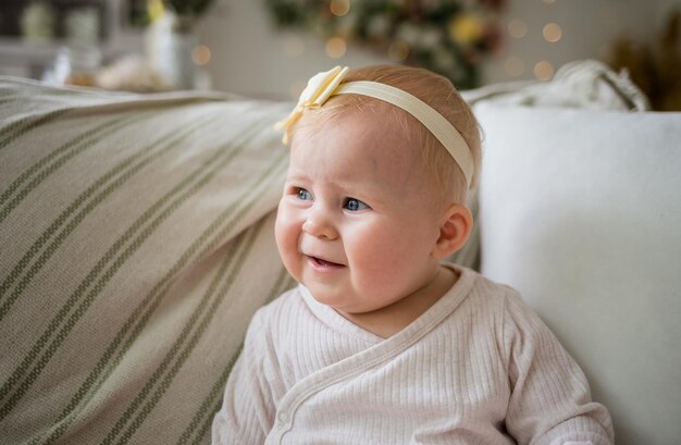 Portert caucasian babe girl in white bodysuit and headband sitting on a sofa in a beautiful room