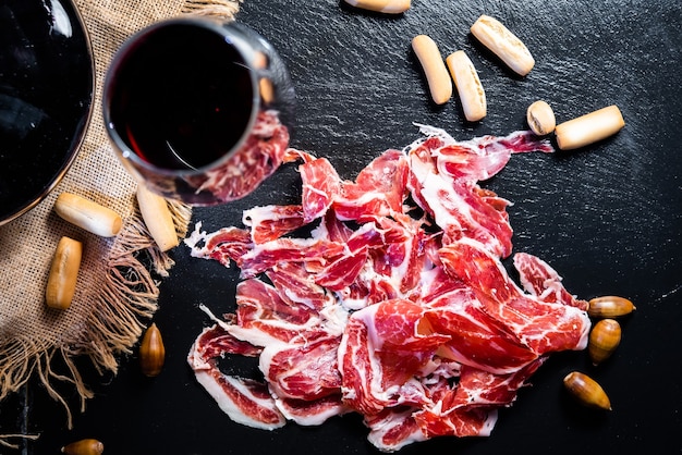 Portie eikelgevoede iberische ham op een zwarte leisteen met een glas rode wijn van bovenaf gezien