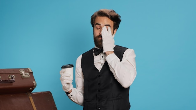 Portier poseert met een koffiekop in de studio, draagt witte handschoenen en voelt zich zelfverzekerd in het werken in de gastvrijheidssector.