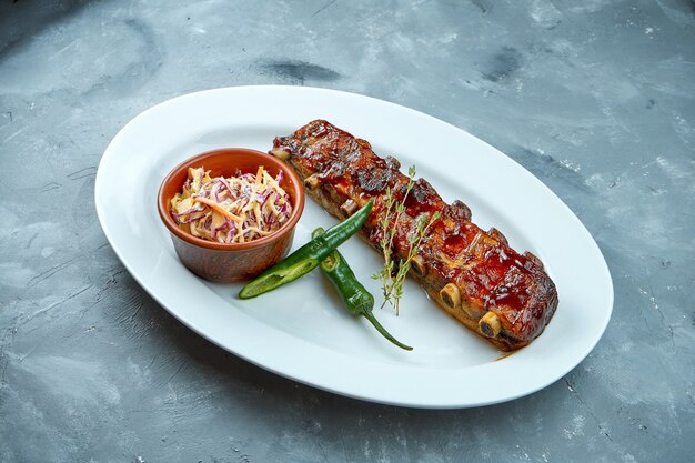 Portion baked BBQ pork ribs with cole slow salad and hot peppers in a white plate