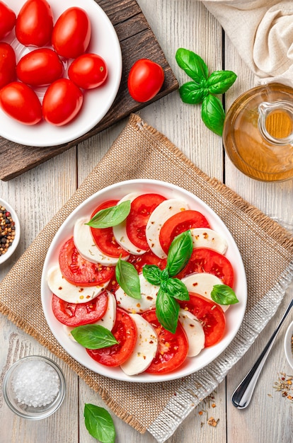 A portion of caprese salad in a white plate on a beige, wooden background. Top view, vertical.