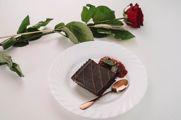 A portion of chocolate cake with strawberry jam and a rose on the table