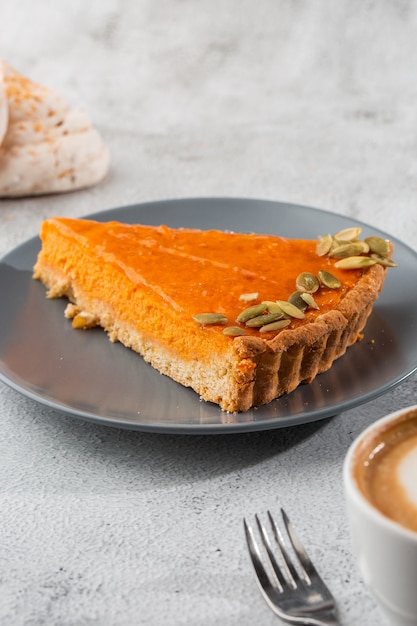 Portion of delicious bright orange pumpkin open pie on gray plate, decorated with pumpkin seeds with dessert forks close-up, top view. Bright marble background. Copy space. Vertical. menu for cafe