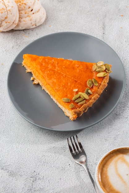 Portion of delicious bright orange pumpkin open pie on gray plate, decorated with pumpkin seeds with dessert forks close-up, top view. Bright marble background. Copy space. Vertical. menu for cafe