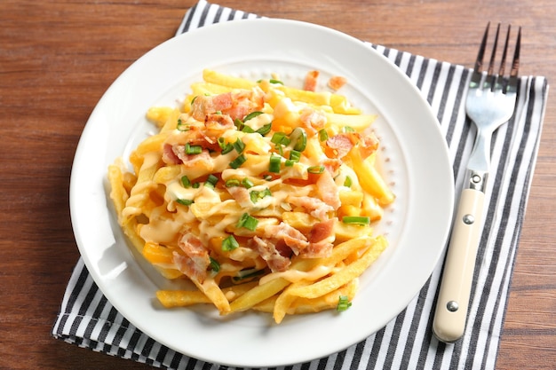 Portion of delicious french fries with bacon and onion on dining table