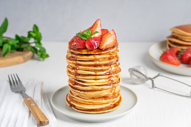 portion of homemade organic pancakes with strawberries and mint topping served in stack with fork