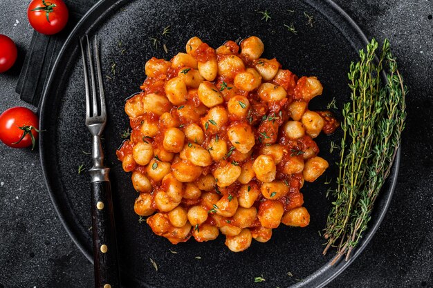 Portion of Italian Gnocchi potato pasta with tomato sauce. Black background. Top view.