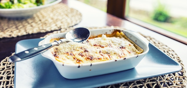 Photo portion of lasagme bolognese in dish on table in restaurant.