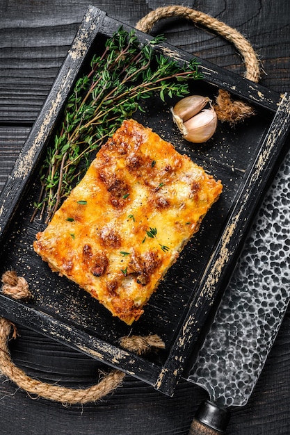 Portion of Lasagna with mince beef meat and tomato bolognese sauce in a wooden tray. Black wooden background. Top view.