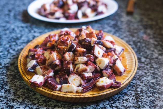 Portion of octopus cut in a wooden plate on a marble background