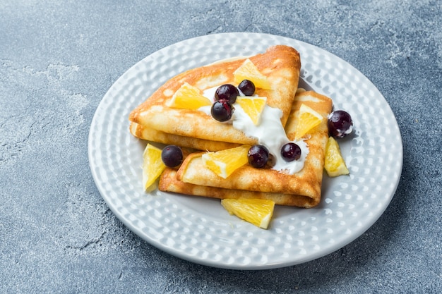 A portion of pancakes with berries and cream on the plate.