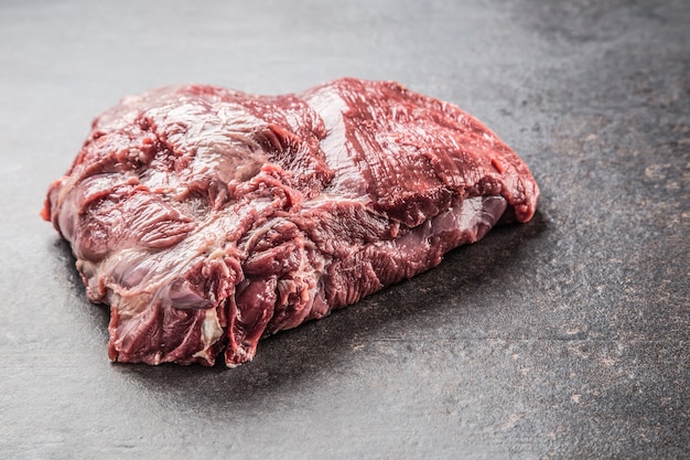 Portion of raw beef neck on dark butcher board.