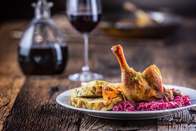 Portion of roast duck leg red cabbage homemade dumplings on plate and red wine on the background.