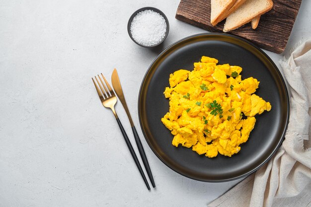 Photo a portion of scrambled eggs with parsley on a gray background. breakfast or brunch. top view, copy space. a recipe for home cooking.