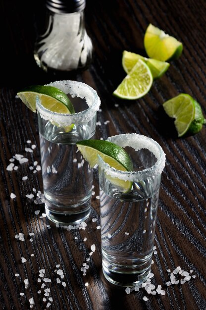 Portion of tequila, framed with a salt edge with slice lime in tall shot glasses