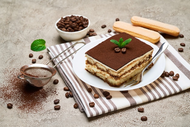 Foto porzione di dessert tiramisù italiano tradizionale e chicchi di caffè sul tavolo di cemento grigio