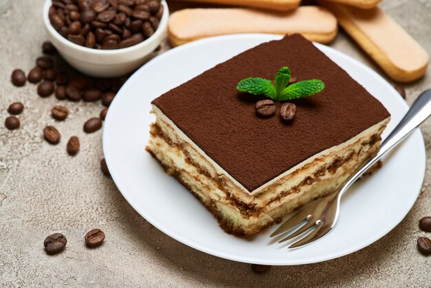 Portion of traditional italian tiramisu dessert and coffee beans on grey concrete table