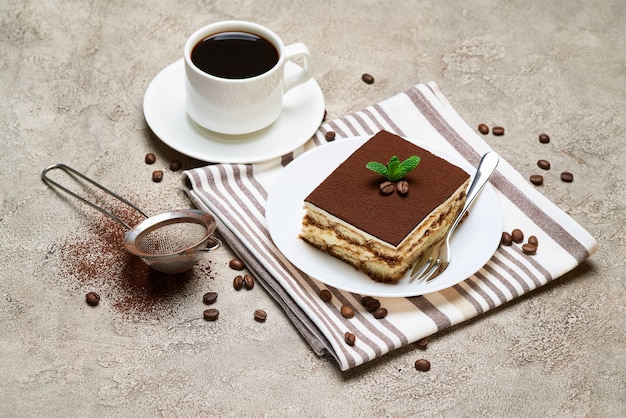 Portion of traditional italian tiramisu dessert and cup of coffee on grey concrete table