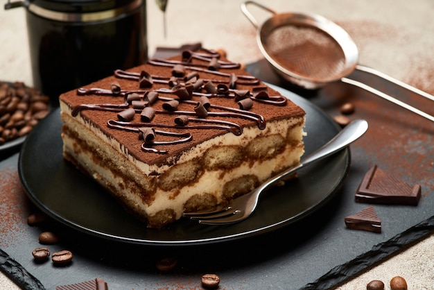 Portion of traditional italian tiramisu dessert and hand coffee grinder on grey concrete table