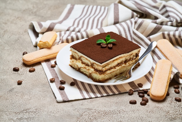 Portion of traditional italian tiramisu dessert and savoiardi cookies on grey concrete table