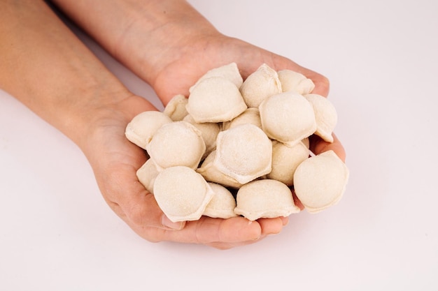 A portion of uncooked pelmeni in hands on white background