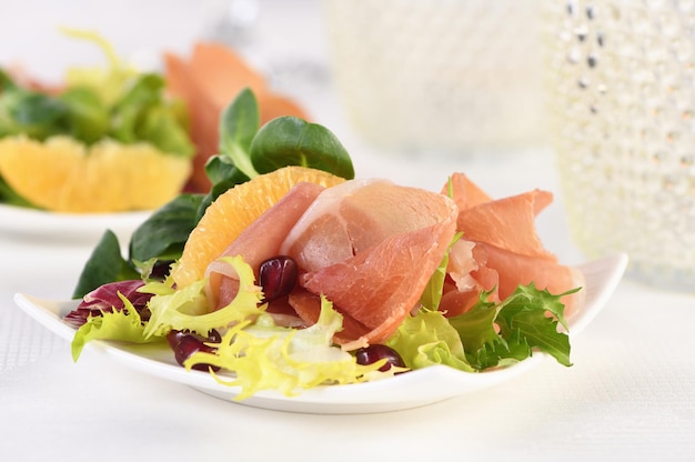 Portioned appetizer of prosciutto ham served on a of mixed with orange and pomegranate