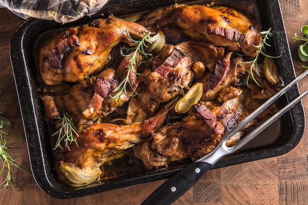 Portioned baked rabbit in a pan with onion rosemary and sauce.