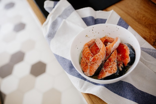 Portions of fresh salmon fillet with aromatic herbs and spices in a bowl on the table in the kitchen
