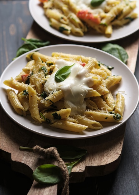 portions of pasta with tomatoes, spinach, parmesan and bolognese sauce on a large kitchen wooden board.