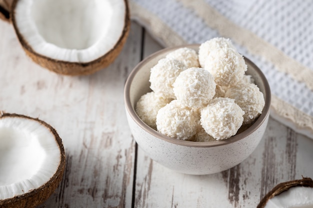 Photo portions of white chocolate coconut candy balls in the bowl, raw cracked coconut