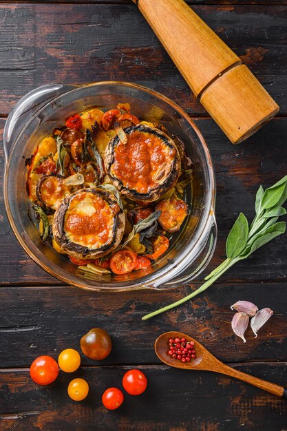 Portobello al forno con formaggio cheddar, pomodorini e salvia in vaso di vetro sulla vista superiore del fondo di legno vecchio.