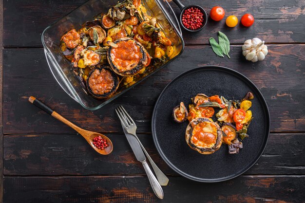 Portobello champignons geserveerd, gebakken en gevuld met cheddar kaas, cherrytomaatjes en salie op zwarte plaat over oude houten donkere achtergrond bovenaanzicht