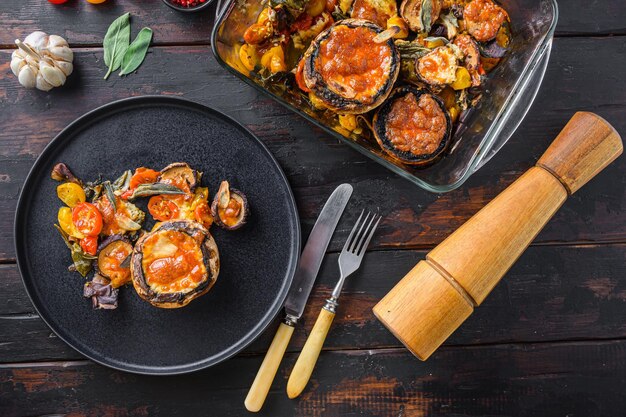 Portobello-champignons geserveerd, gebakken en gevuld met cheddarkaas, cherrytomaatjes en salie op zwarte plaat over oud houten tafelblad.