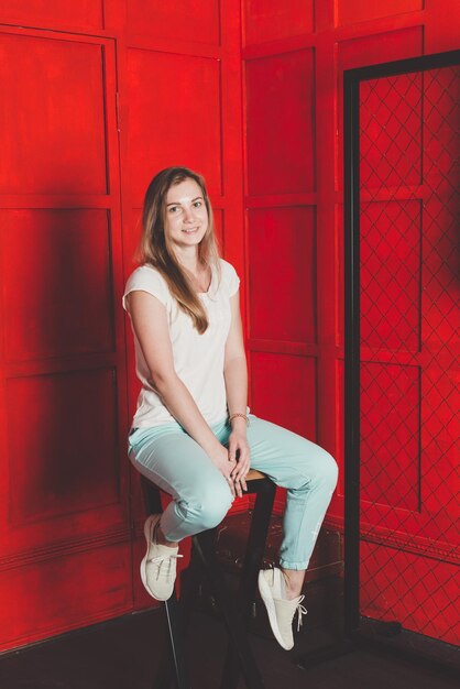 Portraint of woman sits on a chair with red background looks into the camera