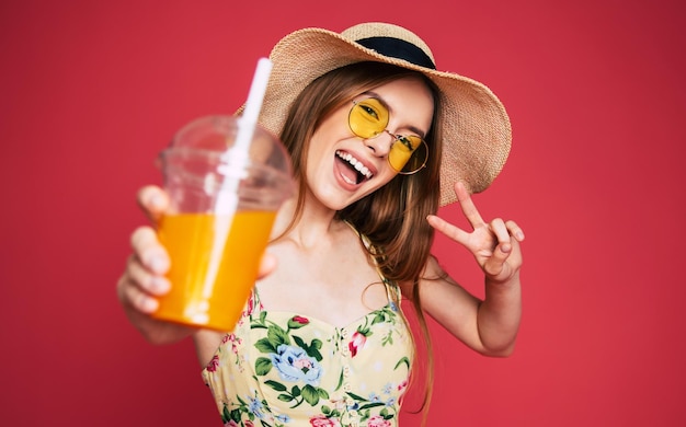 Portrair van blij en opgewonden blonde trendy vrouw in hoed met vers drankje in handen geïsoleerd op roze achtergrond. Zomerstemming